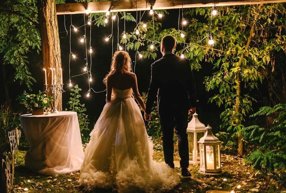 photocall guirlande diy arche couple mariés de dos robe mariage intime lanterne bougie jardin nuit