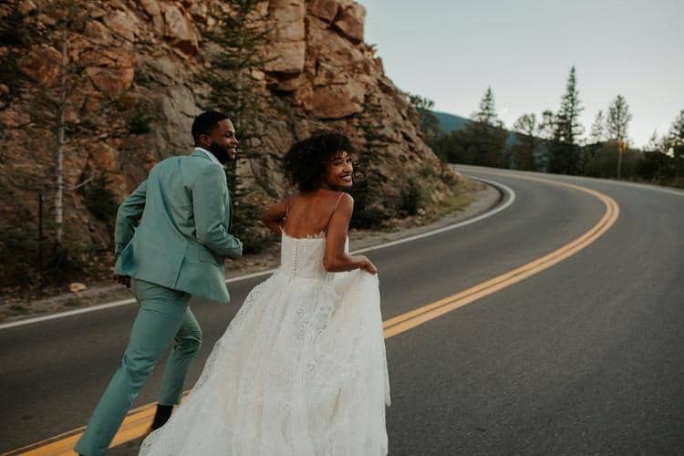 mariage intime à deux couple afro mariés courent sur la route montagne costume vert robes mariée blanche