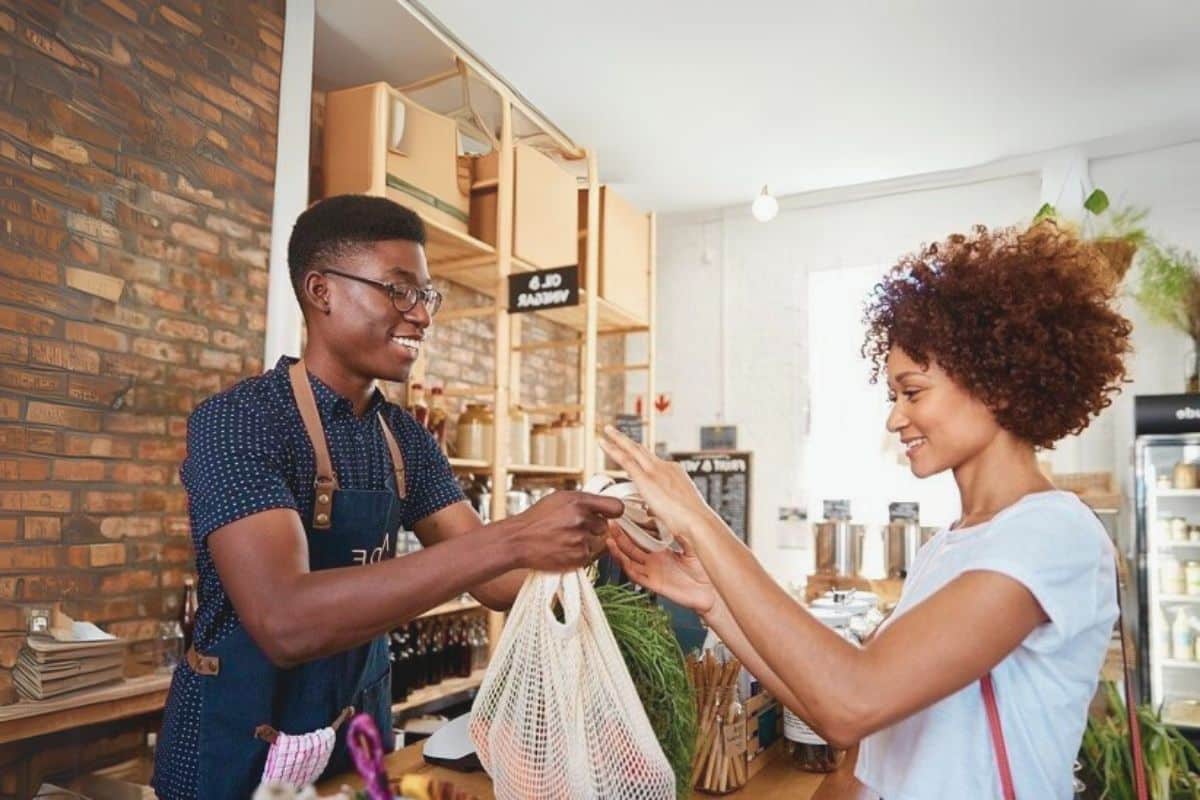 commerçant donne en caisse produit à sa cliente souriante contente transaction