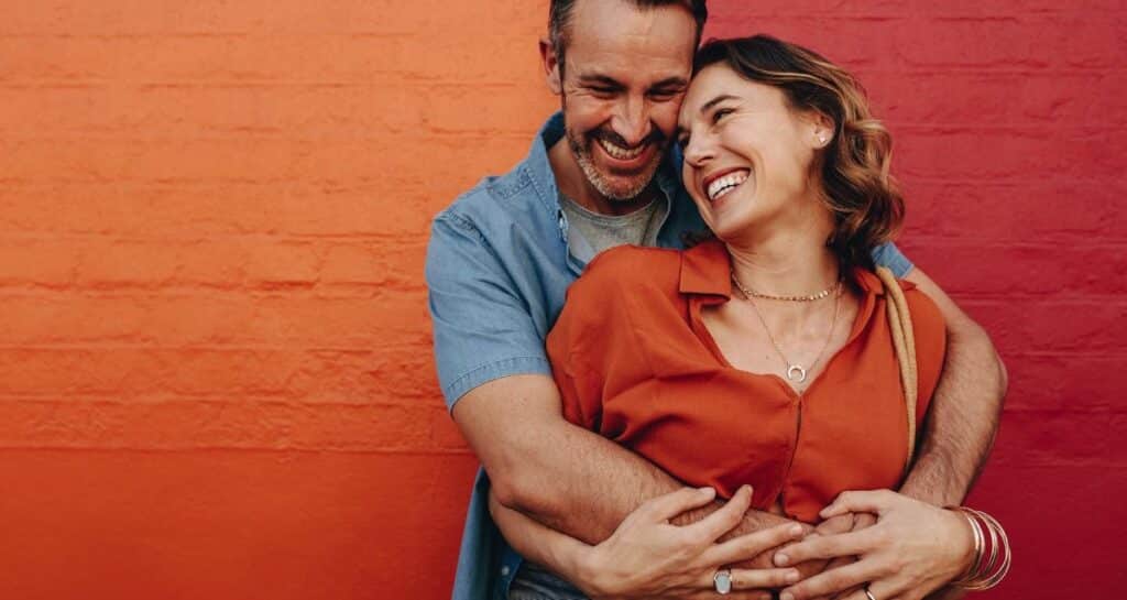 couple mariés enlacés homme et femme adossé à un mur de brique orange rouge heureux