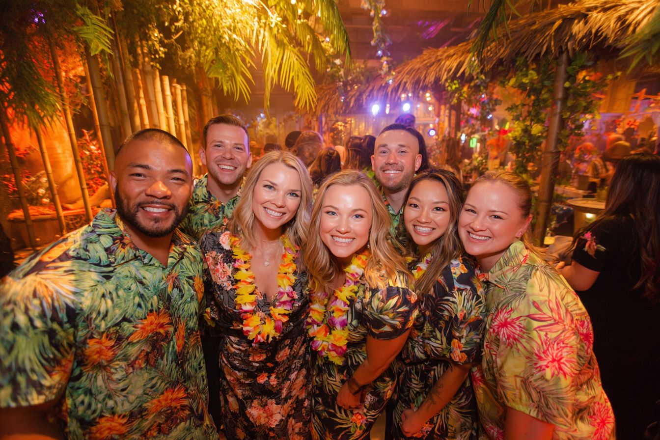 Soirée tropicale d'anniversaire avec bar tiki, palmiers naturels et invités en tenues hawaïennes