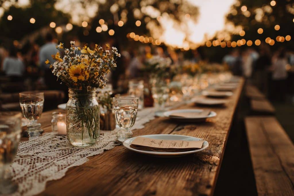 Table mariage champêtre économique décorée avec bocaux wildflowers, guirlandes lumineuses et nappes vintage au coucher solei