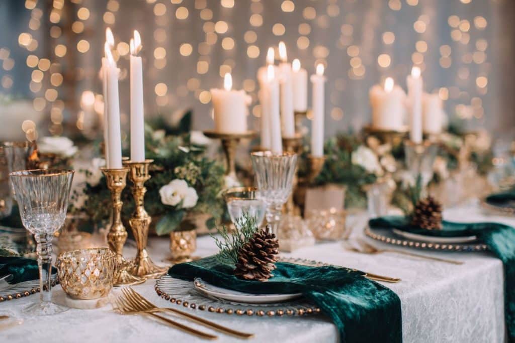 Décoration de table de mariage hivernal élégante avec bougies dorées, branches de sapin, pommes de pin et nappes en velours vert émeraude