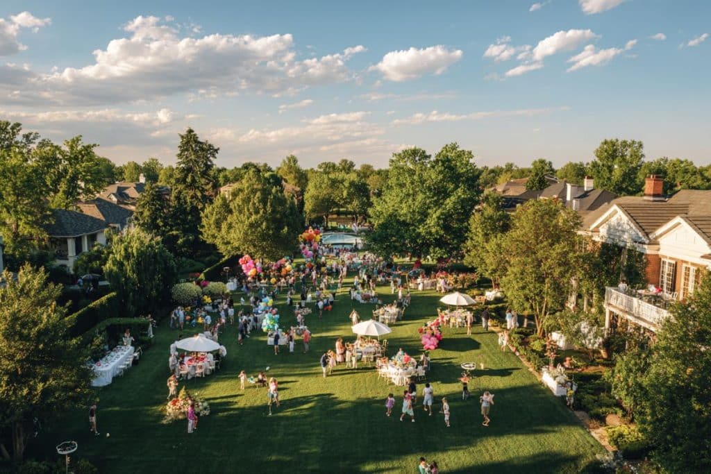 Vue d'ensemble d'une garden party réussie avec nombreux invités dans un grand jardin ensoleillé