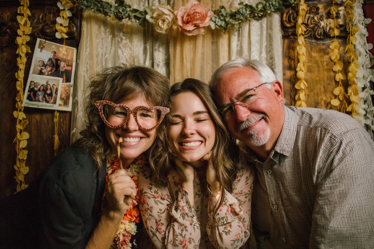 Trois membres d'une même famille posent avec des accessoires dans un photobooth décoré de fleurs pour des noces d'or