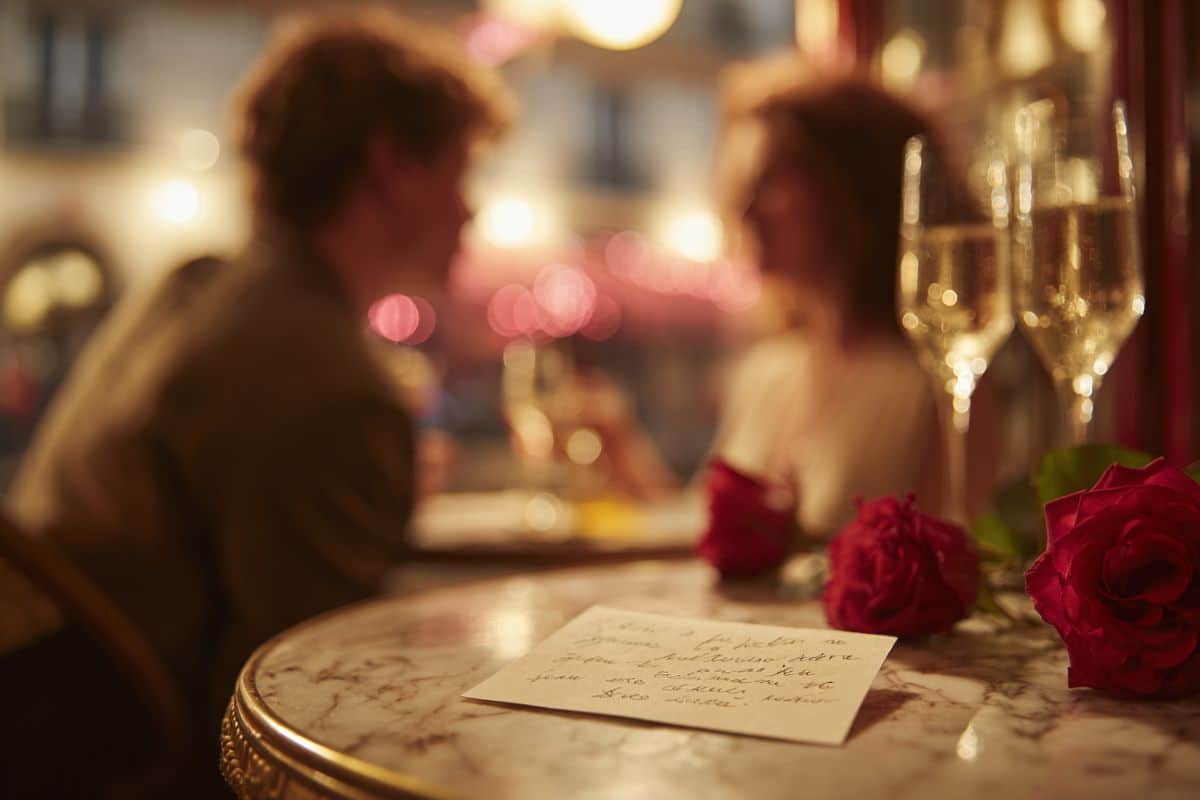 Couple partageant un message romantique pour la Saint-Valentin dans un café parisien avec roses rouges et champagne