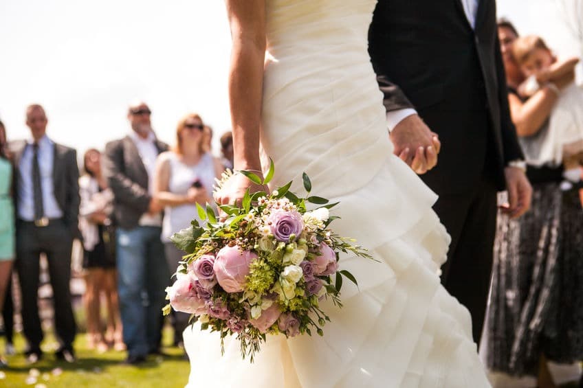 bouquet de la mariée dans sa main avec son mari autour des invité lors de la cérémonie en extérieur