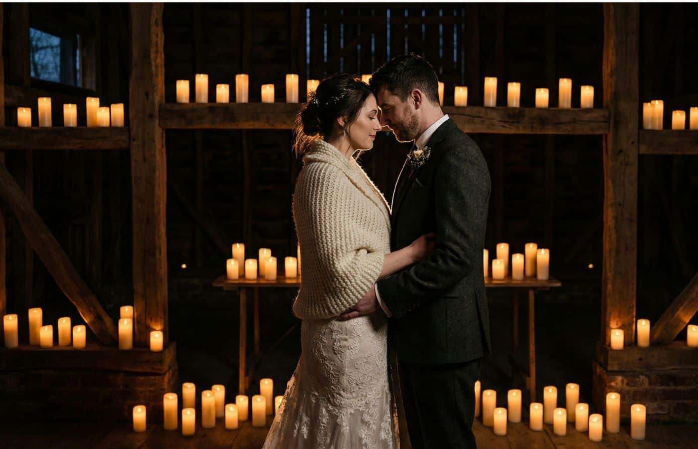 Couple de mariés en clair-obscur dans une grange sombre, entourés de centaines de bougies, style bohème dark et romantique